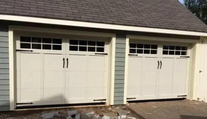 Two garage doors featuring windows, set beneath a sloped roof, showcasing a modern architectural design.