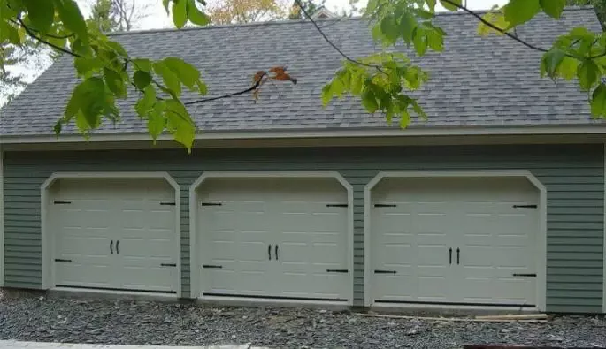 A green garage with three beige garage doors.